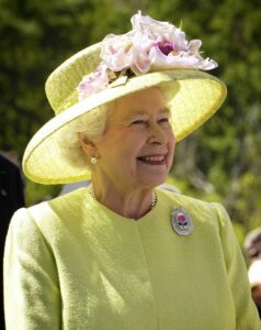 Queen Elizabeth II in a yellow dress and hat with pink flowers