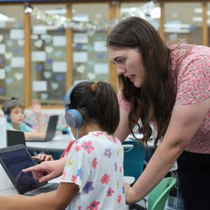 The librarian helps a student on a chromebook.