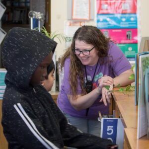 The librarian smiles while helping students find books in the shelves.