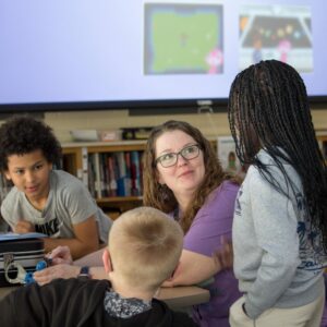 A group of students and Mrs. Broxtermann work together at a table.