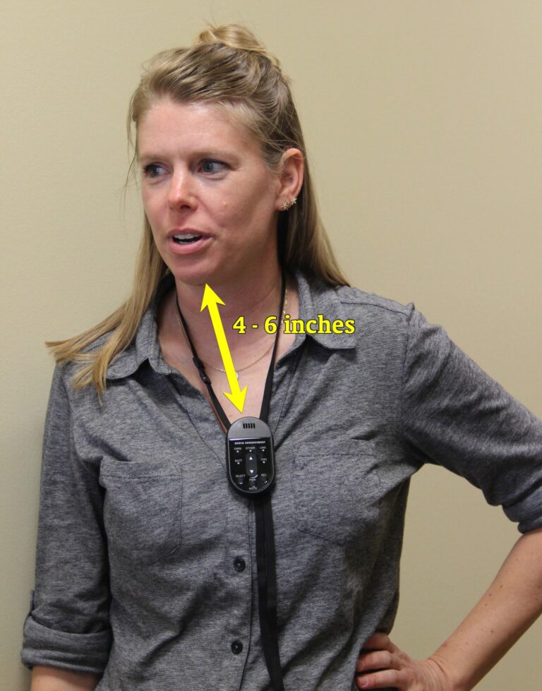 Image of a woman wearing an Audio Enhancement microphone on a lanyard around her neck. A graphic indicates that the mic is approximately 4-6 inches below her chin, an ideal placement.