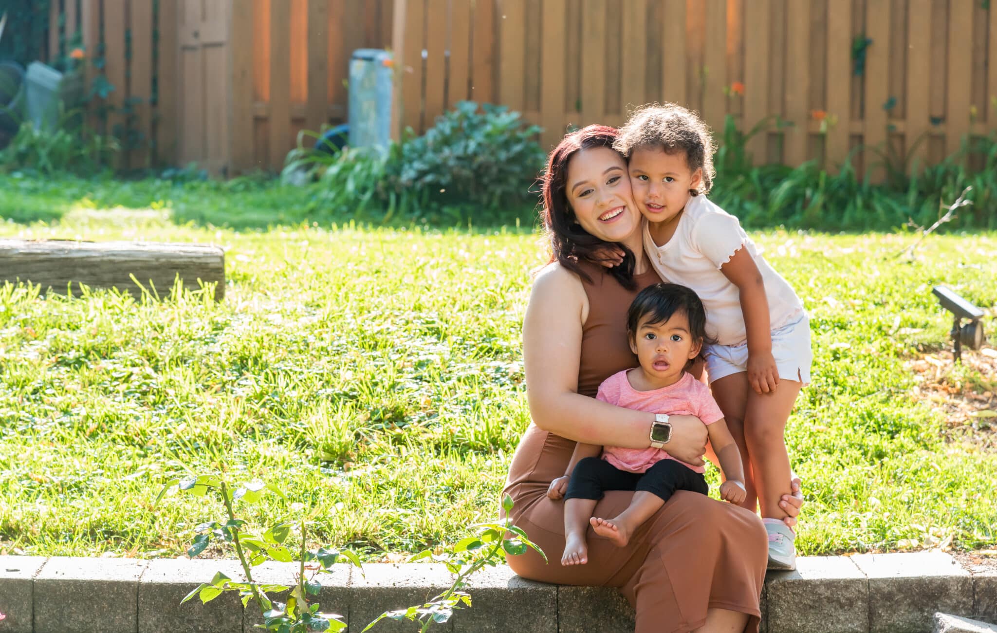 A woman sits on a short wall with two children