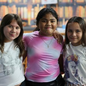 Three friends in the library smile at the camera.