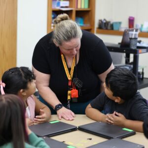 Mrs. Anderson talks to students working on a project at their table.
