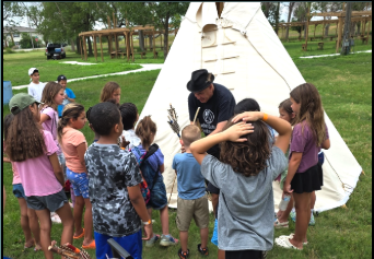 Group of students listening to an elder in front of a tipi