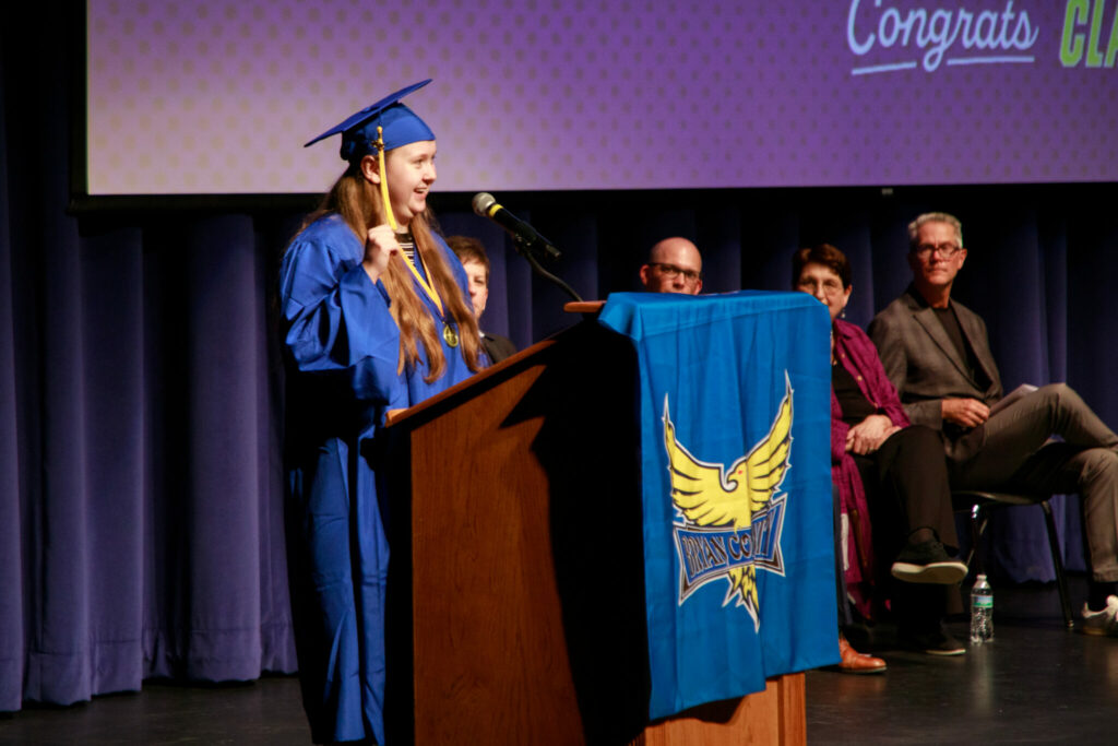 Student in a blue graduation cap speaking at a podium