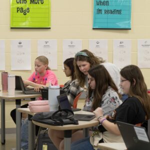 A librarian points to a student's screen while teaching a class