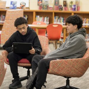 Two students sitting in the library on comfy chairs.