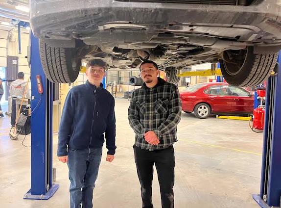 From left, a father and son stand underneath their car that is on a lift in Northeast's auto shop. They are preparing to do an oil change on their vehicle.