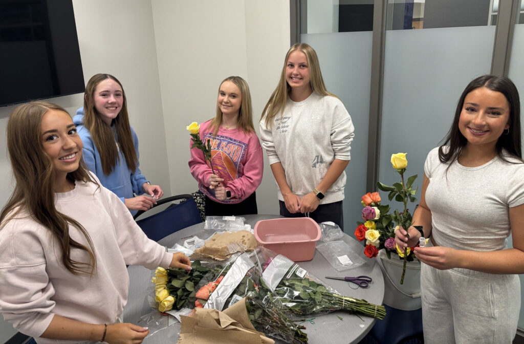 Five Standing Bear High School students stand around a table that is filled with several bouquets of roses. The five girls are preparing to pass out the roses to staff members as part of Hope Squad activity.