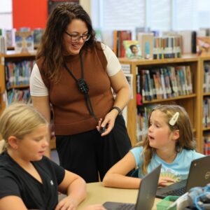 The librarian smiles with two students at a table.