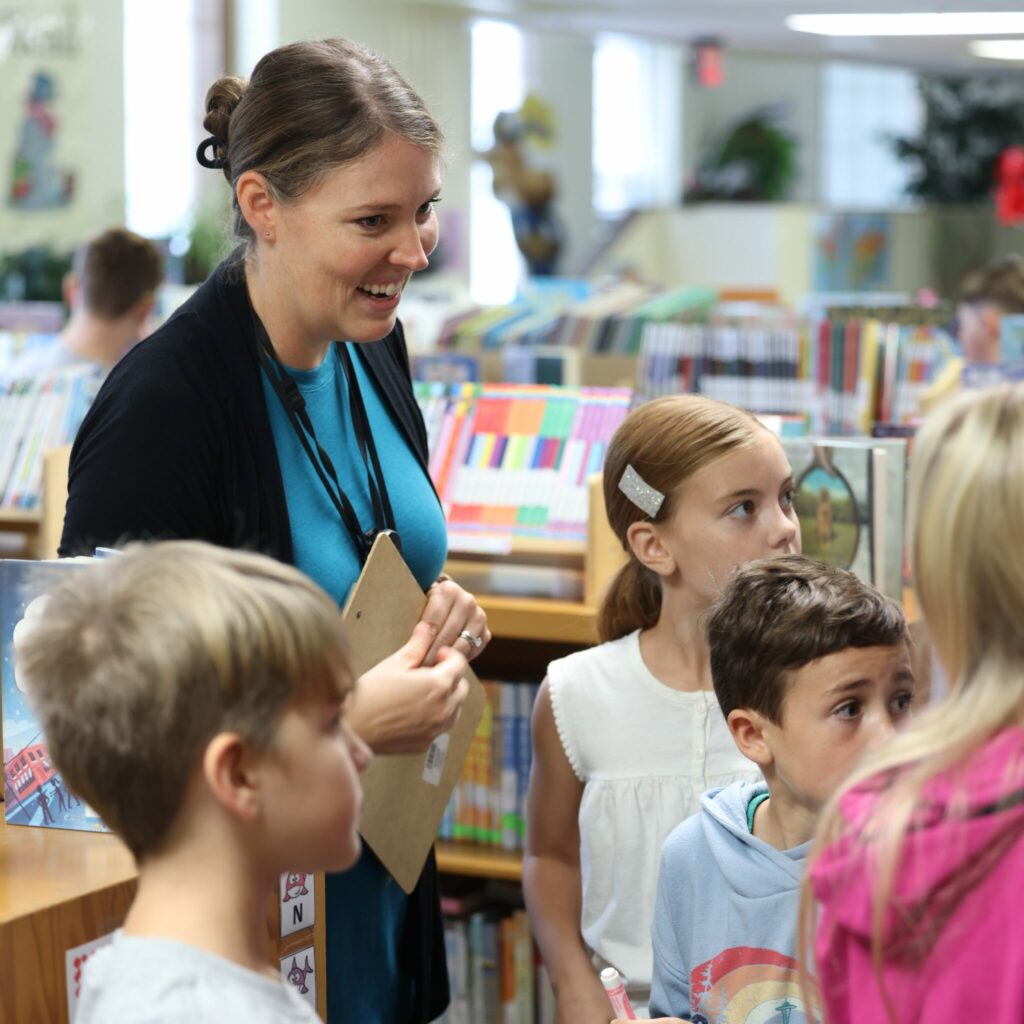 A librarian smiles at students in the shelves