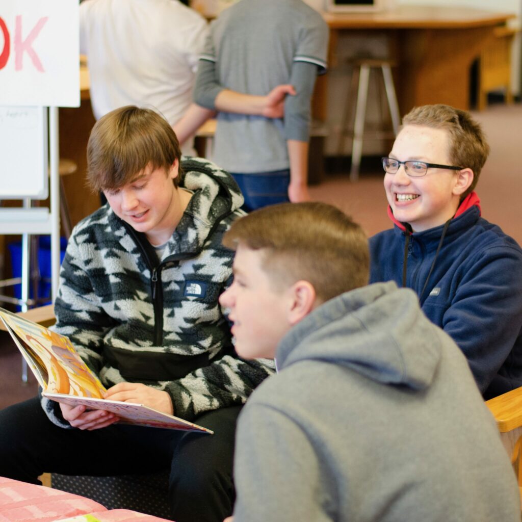 Three students sit together smiling while looking at a book