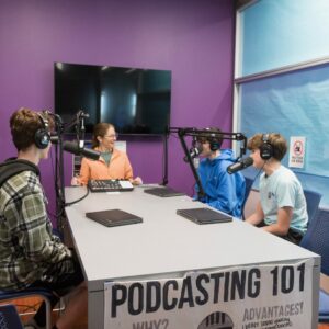 The librarian demonstrates how to use the podcast equipment for students.