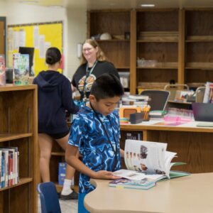 A student checks out a book while another looks through a book.