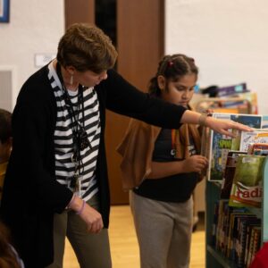 Mrs. Reda and a student look for a book in a book cart.