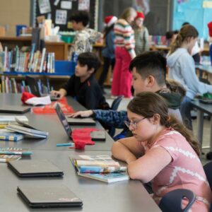 A group of students read at a table while others check out books.
