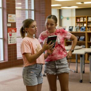 Two students discuss a book in the library.