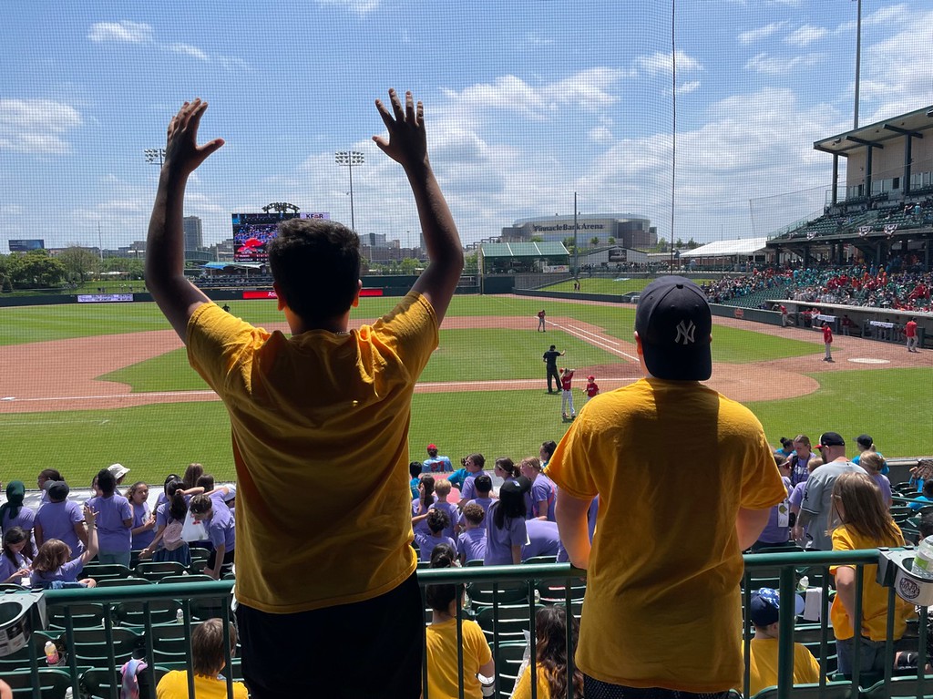 Two students in yellow shirts watch the ballgame from the concourse