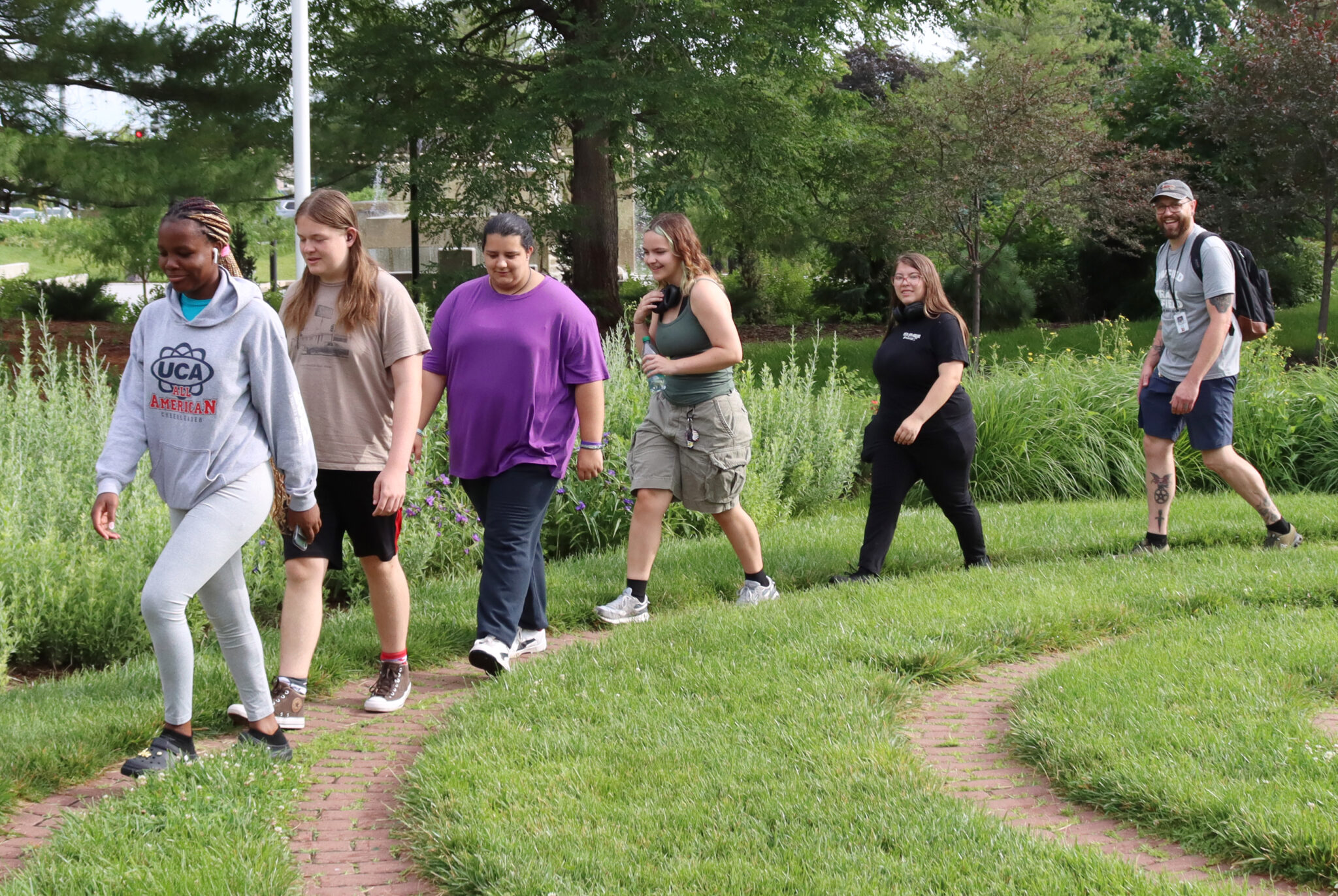 Five students and a teacher walking along a path in the grass at the sunken gardens