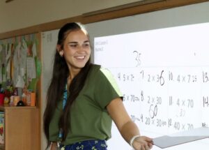 A college student stands in front of a projector screen filled with numbers pointing some out