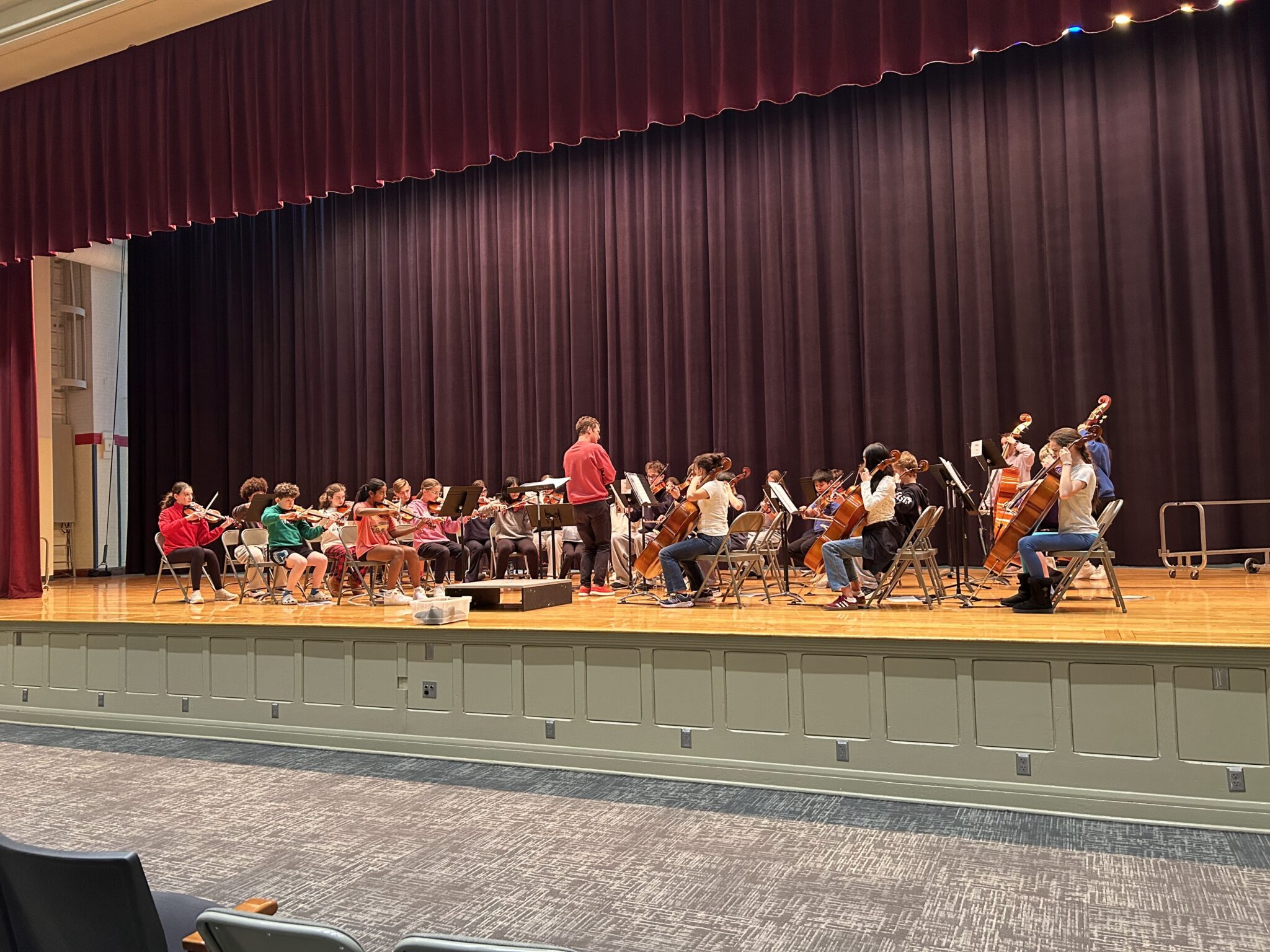 A large group of string players sit on a stage